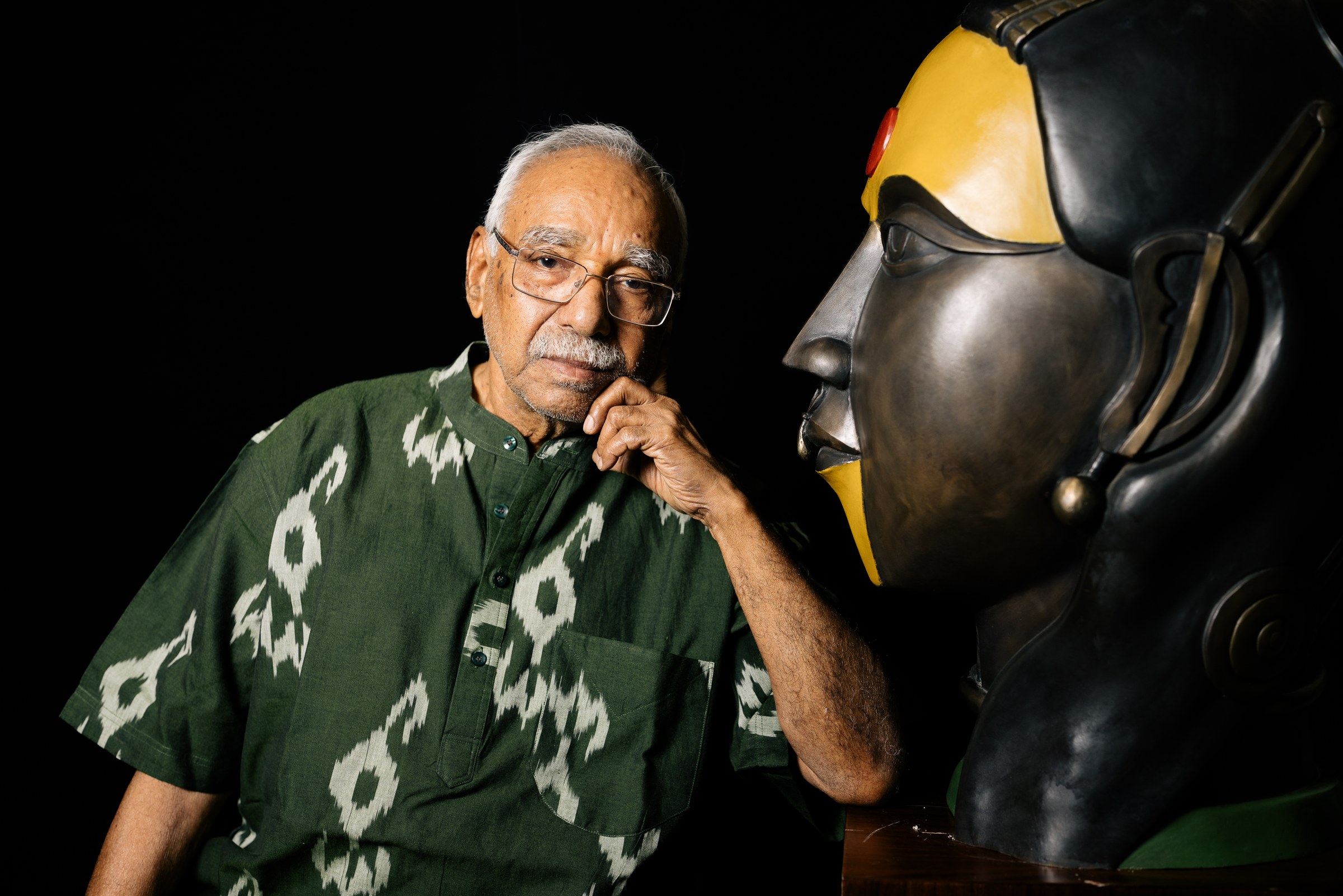 Thota Vaikuntam resting his chin on his hand beside a large bronze head in profile, black background